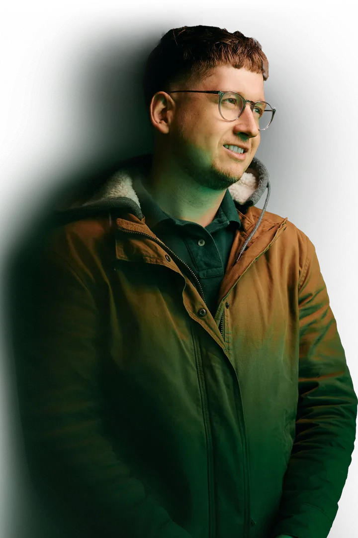 Max Onyx in a brown jacket, looking to the side and smiling